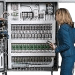 A woman in blue is looking at the buttons on an electrical panel.