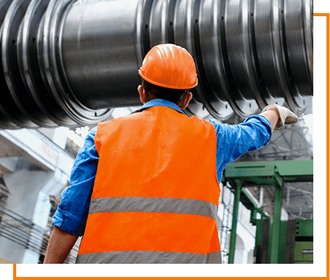 A man in an orange vest and hard hat standing next to a large metal object.