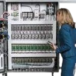 A woman in blue is looking at the buttons on an electrical panel.